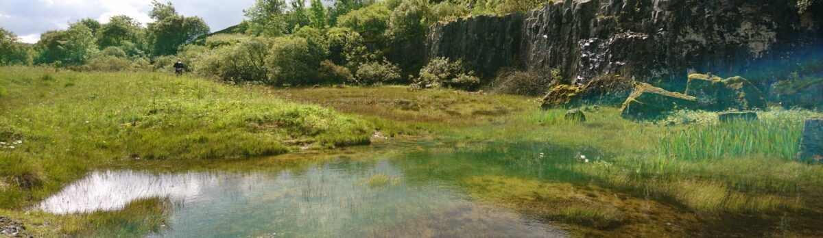 a flooded quarry with small rock cliffs to one side and grass to the other